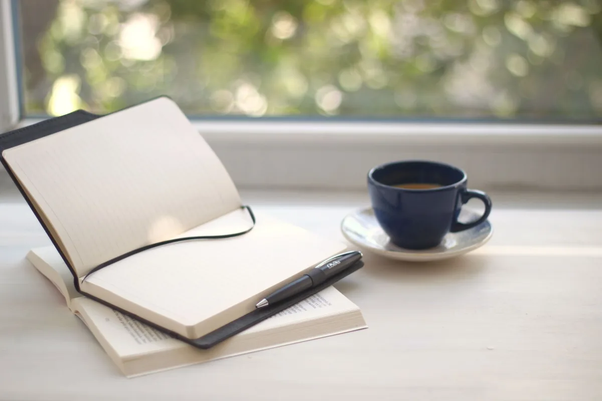Open notebook, pen and book on a bright desk by a sunlit window